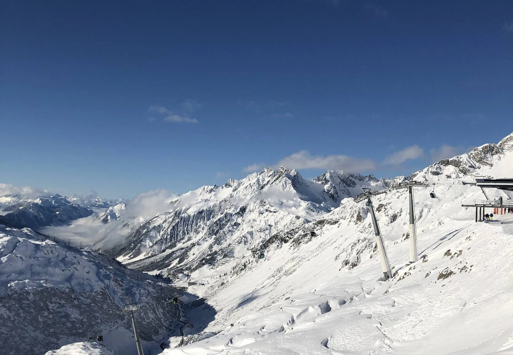 Verschneite Gipfel unter tiefblauem Himmel, präparierte Piste im Vordergrund
